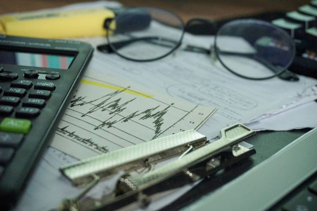 A stockbroker's desk, with the stock market open on the computer and a calculator on the table, performing calculations and analysis.